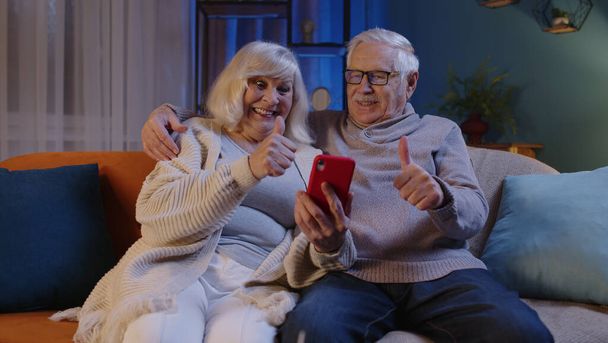 シニアカップル祖父祖母作るオンラインショッピング上の携帯電話で自宅ソファに座って - 写真・画像