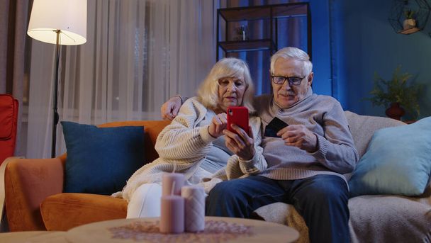 Couple de personnes âgées avec smartphone à la maison, faire des achats en ligne avec des cartes bancaires en plastique de crédit - Photo, image