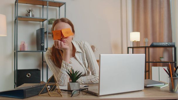 Mujer cansada maestra usando ordenador portátil con pegatinas divertidas en los ojos duerme en el lugar de trabajo, siesta - Foto, Imagen