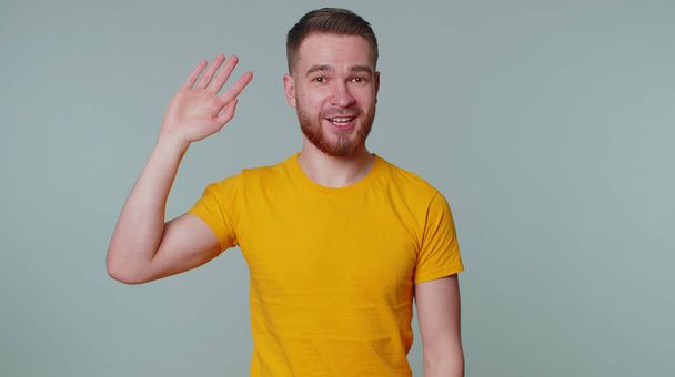 Γενειοφόρος άντρας χαμογελά φιλικός στην κάμερα και κουνάει τα χέρια του χαιρετώντας ή χαιρετώντας, καλωσορίζοντας - Φωτογραφία, εικόνα