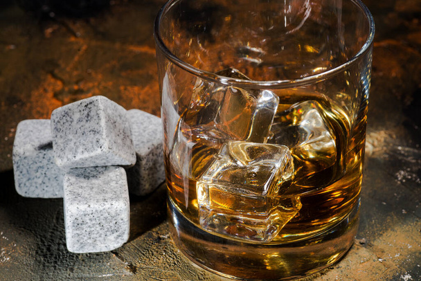 Whiskey with whiskey stones. Glass of whiskey in glass cup with ice cubes on brown background - Fotó, kép