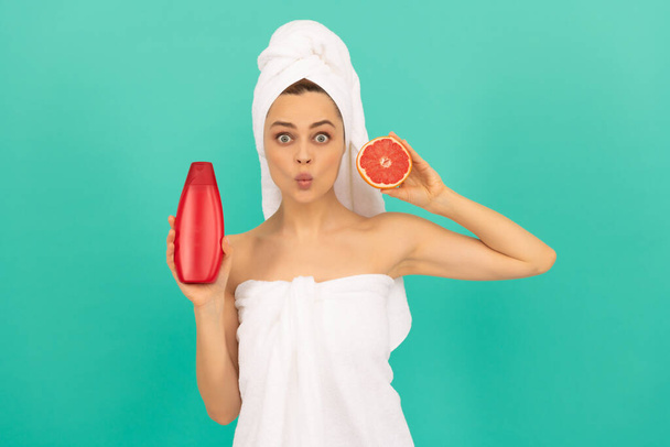 verbaasd vrouw met grapefruit shampoo fles op blauwe achtergrond - Foto, afbeelding