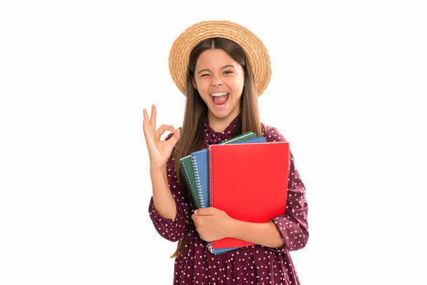 счастливый подмигивающий ребенок держать школьный учебник для обучения изолированы на белом шоу ОК жест, ОК. - Фото, изображение