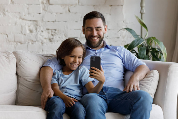 Papà suo figlio siede sul divano divertendosi con lo smartphone - Foto, immagini
