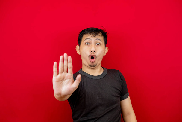 Retrato del emocionado hombre asiático con camiseta negra de pie sobre fondo rojo, mostrando un gesto de cinco dedos mientras se abre la boca. Concepto de anuncio y recordatorio. - Foto, imagen