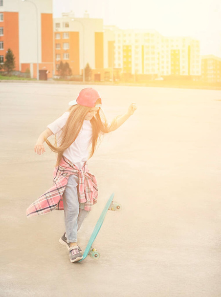 A teenage girl with long hair on a skateboard jumps on the street .Soft focus in the sun - Fotoğraf, Görsel