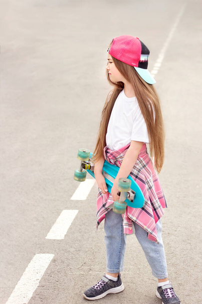 a teenage girl with a skateboard in her hands stands sideways on the asphalt close-up - Foto, afbeelding