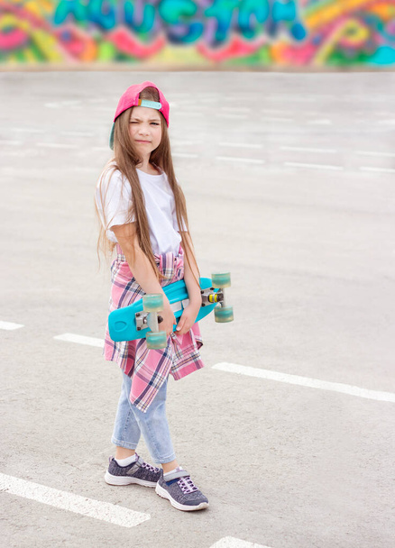 little smiling girl stands on the street with a skateboard in her hands - Foto, afbeelding