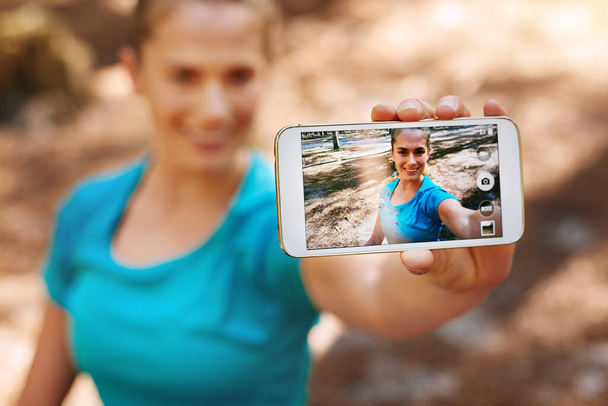 Ik neem een selfie voor mijn selfie. Shot van een sportieve jonge vrouw met behulp van haar mobiele telefoon, terwijl uit in de natuur. - Foto, afbeelding