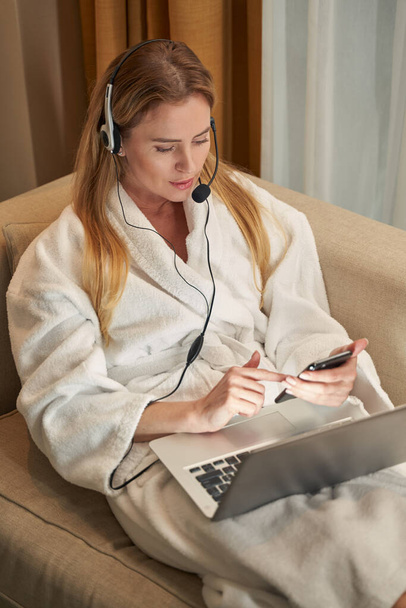 Working woman in headset with laptop using smartphone - Fotó, kép