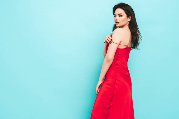High fashion portrait of young beautiful brunette woman wearing nice trendy red evening dress. Sexy fashion model posing in studio. Fashionable female isolated on blue - Fotoğraf, Görsel