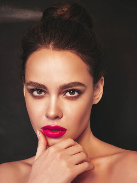Fashion beauty portrait of young brunette woman with evening stylish  makeup and perfect clean skin. Sexy model with hair in a bun posing in studio near black wall. With pink bright natural lips - Foto, Imagen