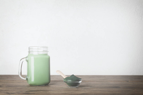 fresh green smoothie in glass bottle and spirulina powder with spoon on wooden background. useful habits - Foto, immagini