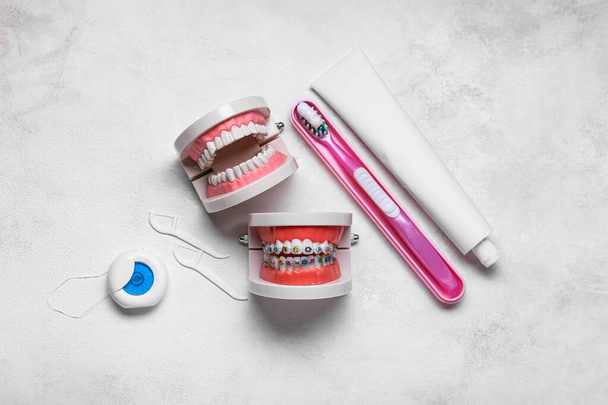 Modelo de mandíbulas com aparelho, escova de dentes, fio dental e colar em fundo claro - Foto, Imagem