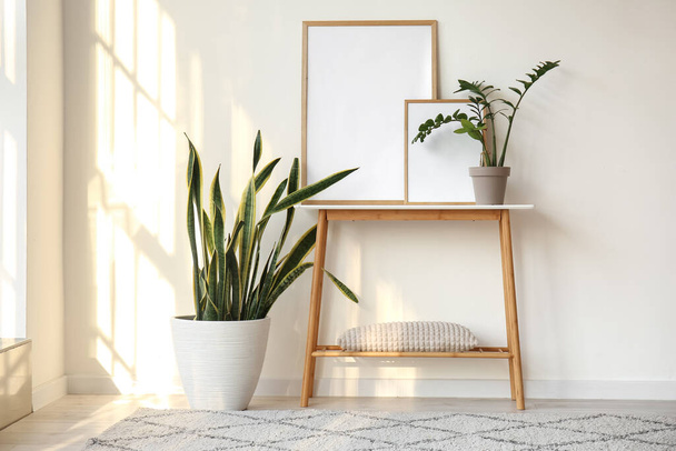 Пустые рамы на столе и комнатные растения возле белой стены - Фото, изображение