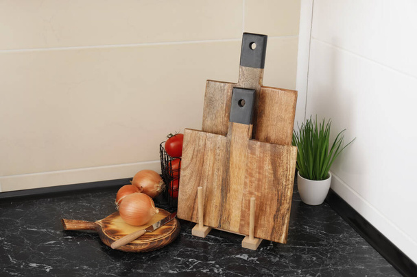 Wooden cutting boards, houseplant and fresh vegetables on table near light tile wall - Photo, Image
