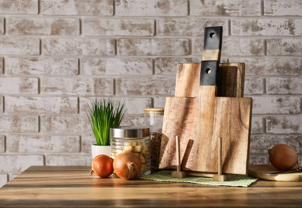 Placas de corte de madeira, frascos com produtos, planta de sala e cebola na mesa perto da parede de tijolo - Foto, Imagem