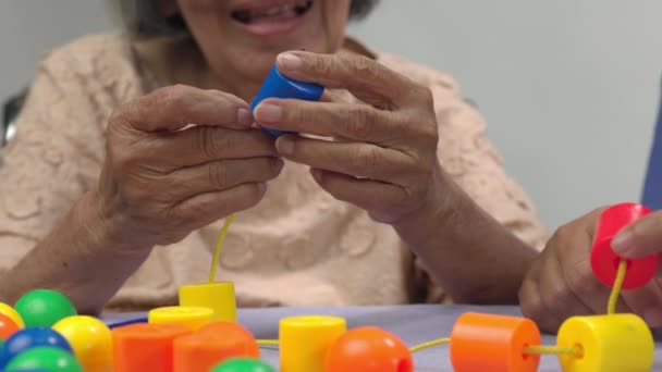 Caregiver and senior woman playing stringing beads game for dementia prevention - Footage, Video