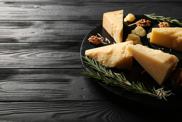 Board with pieces of tasty Parmesan cheese on black wooden background, closeup - Foto, afbeelding
