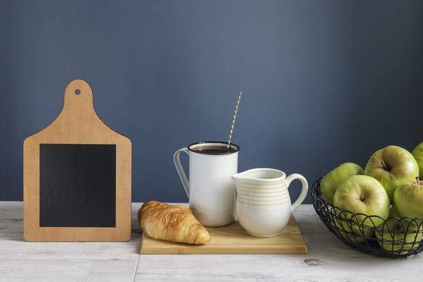 Coffee cup and croissant with chalkboard sign on wooden table. Chalkboard mock up background for design. Dark blue background. Copy space - Фото, зображення