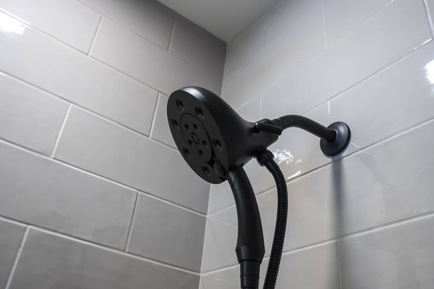 Close up, low angle view of a modern black detachable shower head in a white tiled bathtub - Photo, Image
