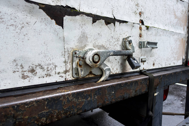 Vista angular de perto de uma trava de metal enferrujado na parte de trás de um caminhão em movimento branco, com uma escada preta - Foto, Imagem