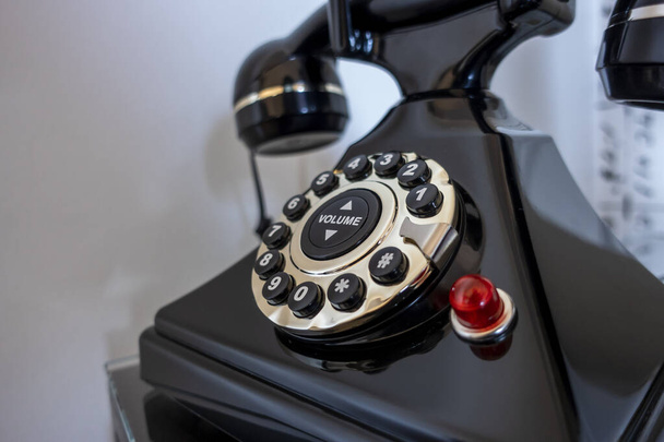 Γωνία επιλεκτική εστίαση σε ένα μαύρο περιστροφικό τηλέφωνο σε ένα κομοδίνο υπνοδωμάτιο, πυροβόλησε σε ένα λευκό φόντο - Φωτογραφία, εικόνα