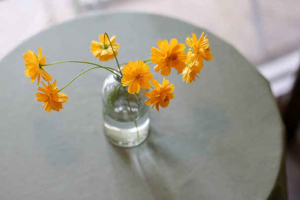 selectieve focus geel-oranje bloemen Hoge hoek in een glazen vaas geplaatst op een tafel ingericht in een vintage coffeeshop. Restaurant concept op een dag zonder klanten eenzaam dag - Foto, afbeelding