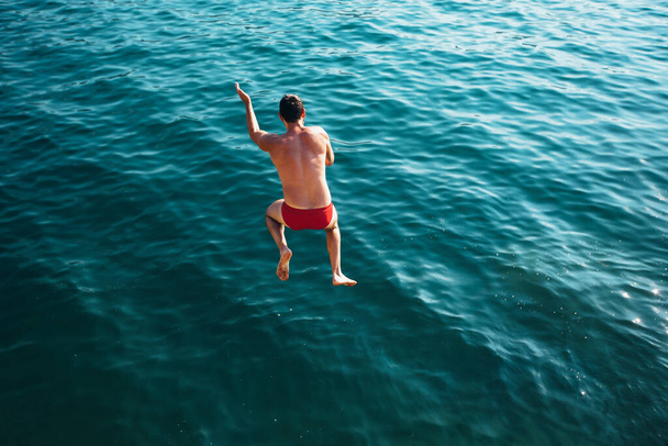 Man jumping off cliff into the sea. Summer fun lifestyle. - Фото, изображение
