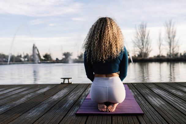 blonde cheveux bouclés femme sur le dos sur ses genoux au coucher du soleil, yoga de relaxation - Photo, image