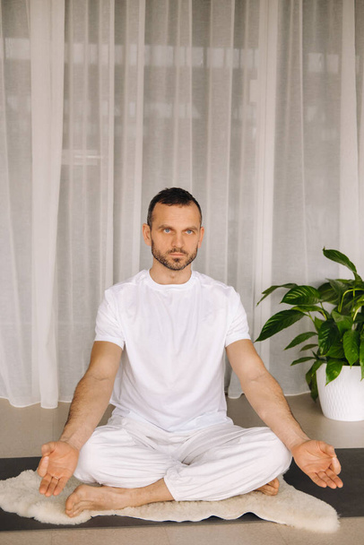 a man in white sportswear is doing yoga with a fitness room. the concept of a healthy lifestyle. - Фото, зображення
