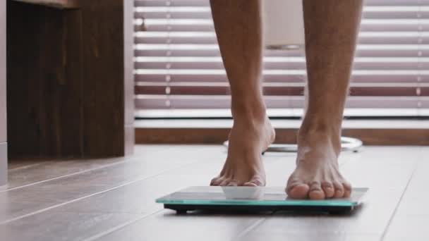Lähikuva uros jalat hoikka ohut urheilullinen tunnistamaton kaveri mies urheilija seisoo kotona kylpyhuone kävely paljain jaloin sähköisen asteikot tarkistaa paino laihtumiseen kehon valvonta kiloa urheilu lihotus - Materiaali, video