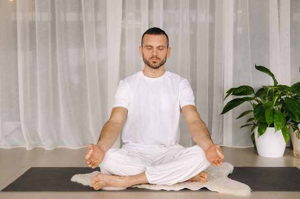 a man in white sportswear is doing yoga with a fitness room. the concept of a healthy lifestyle. - Фото, зображення