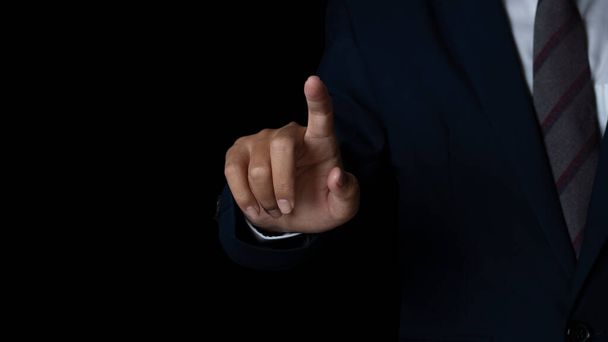 Молодой бизнесмен показывает пальцем на черном фоне экрана. копировальное пространство. - Фото, изображение