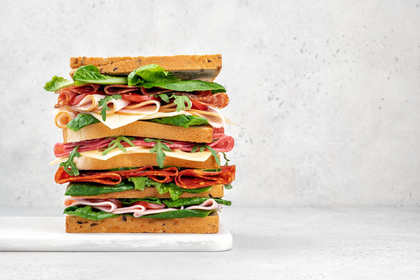 Big tasty sandwich with ham, salami, salad, cheese and tomatoes - Foto, afbeelding