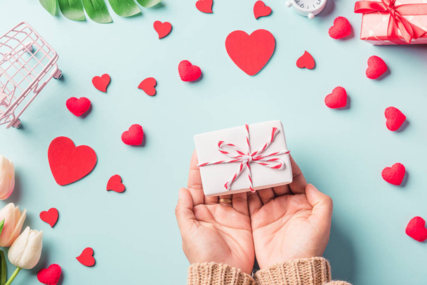 Valentine's day and birthday. Woman hands holding gift or present box decorated and red heart surprise on blue background, Female's hand hold gift box package in craft paper Top view flat lay - Fotografie, Obrázek