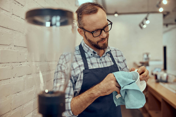 Trabajador masculino barbudo limpiando taza de café en la cafetería - Foto, imagen