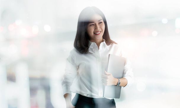 Sonriente de asiático activa moderna mujer de negocios con el ordenador portátil en la mano en la oficina. - Foto, imagen