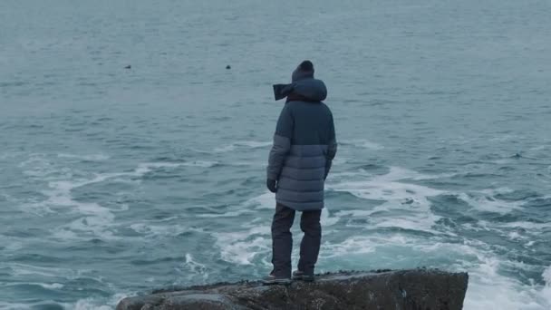 Чоловік стоїть на камені і дивиться на морські хвилі. Поняття самотності та відображення. Вид ззаду. Повільний рух
 - Кадри, відео