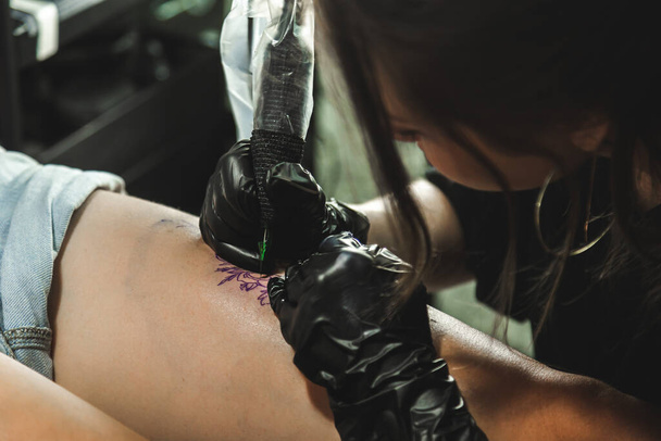 Professional female tattoo artist makes a tattoo in the studio, close-up. Dark photography - Foto, afbeelding