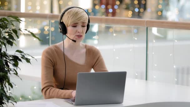 Middle aged adult 40s business woman in headset microphone talking at laptop web camera consultation online distant remote teacher coach helpline agent manager tutor advise video call conference chat - Footage, Video