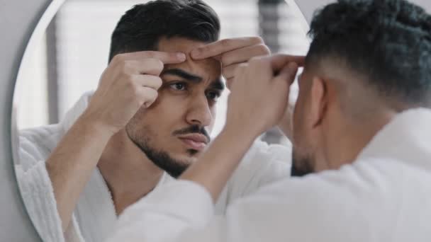 Homme arabe arabe arabe barbu malheureux regardant dans le miroir de salle de bain se sentant inquiet au sujet de l'acné problème de peau faciale. Homme millénaire anxieux serrant bouton toucher visage frustré points noirs soins de la peau - Séquence, vidéo