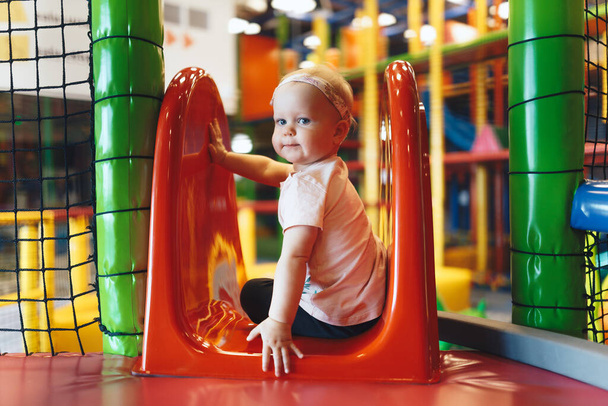 Podekscytowana dziewczynka bawiąca się na zjeżdżalni w parku rozrywki. Cute baby girl gra na kolorowym placu zabaw w przedszkolu  - Zdjęcie, obraz