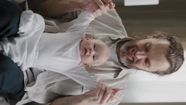 Вертикальний вигляд бородатий батько тато з маленькою дочкою син дитина вдома грає весело проводячи час разом тато тримає немовля новонародженого руками піднімає кавказьке сімейне виховання дітей
 - Кадри, відео