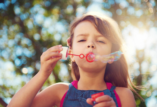 Keep calm and blow bubbles. Shot of a cute young girl blowing bubbles outside. - Zdjęcie, obraz