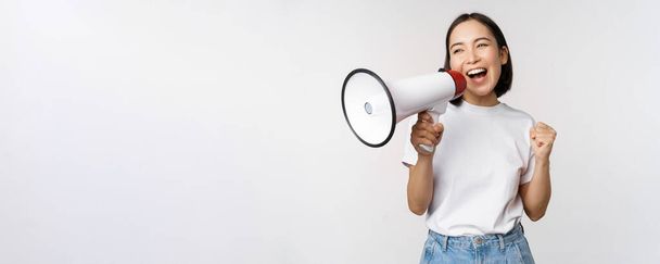 Chica asiática gritando al megáfono, joven activista protestando, usando altavoz, haciendo anuncio, fondo blanco - Foto, Imagen