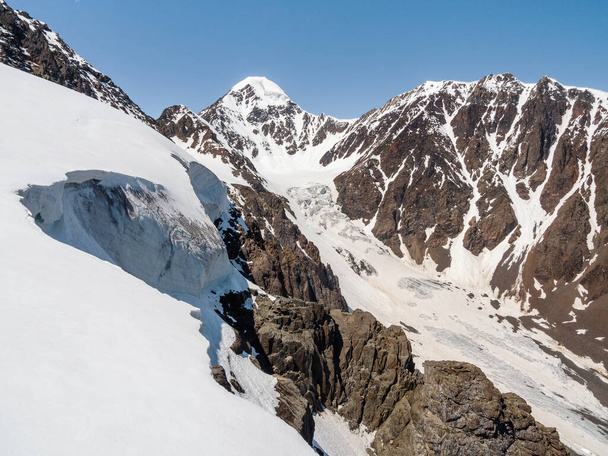 Śnieg nad przełęczą. Widok na zaśnieżone zbocze po drodze do przełęczy w górach. Duży lodowiec Aktru, wysoko w górach, pokryty śniegiem i lodem.  - Zdjęcie, obraz