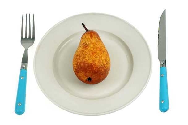 Concetto di dieta con una pera in un piatto e posate su uno sfondo bianco - Foto, immagini