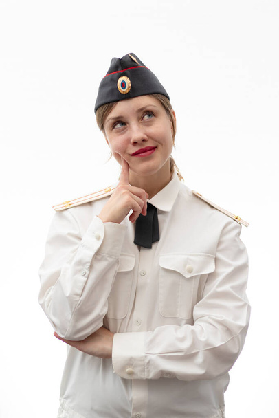 Una hermosa joven oficial de policía rusa vestida de uniforme con una gorra y una camisa blanca sonríe sobre un fondo blanco. Enfoque selectivo. Retrato - Foto, imagen