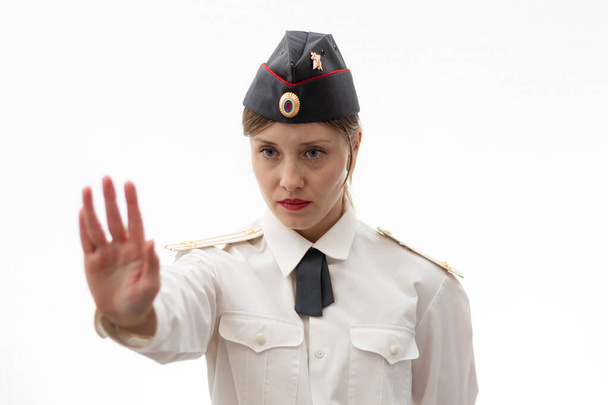 Hermosa joven oficial de policía rusa en uniforme de vestir muestra una señal de stop con sus manos sobre un fondo blanco. Enfoque selectivo. Retrato - Foto, imagen